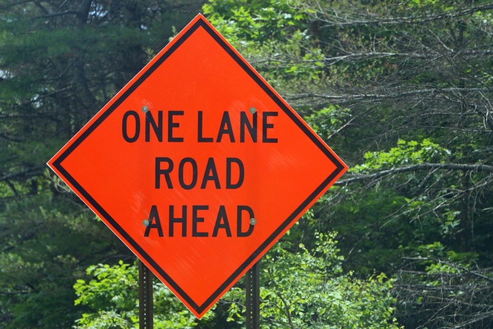 A one lane road ahead sign in front of trees